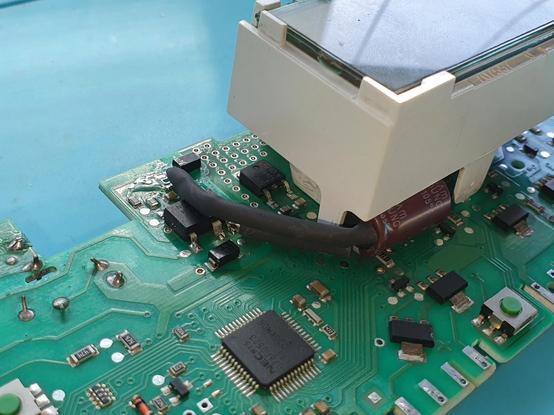 Imaxe dunha placa de control de lavadora, onde se ve un condensador electrolítico cilíndrico metido debaixo dunha peza de plástico que sostén a pantalla LCD, e cos seus terminais aislados con trozos de tubo termorretráctil (sen axustar).