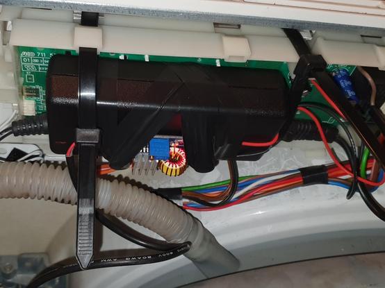 Imaxe da placa de control instalada na lavadora. Ten enriba unha fonte de alimentación rectangular e negra, suxeita con unhas bridas. Hai un conversor DC-DC unido á fonte de alimentación con cinta aislante.