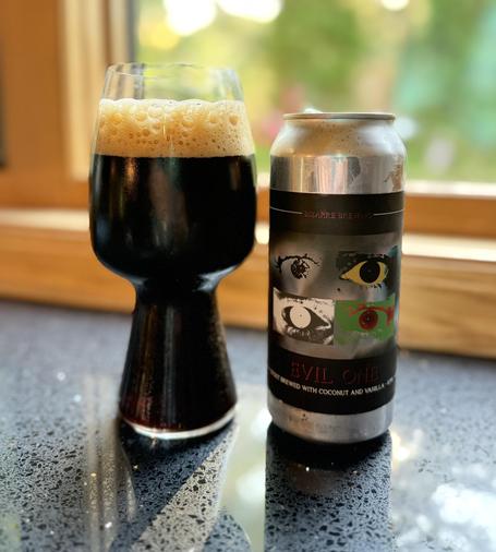 A stout glass of dark beer next to a silver pint can with a black label that has four eyes in various colors and painted treatments.