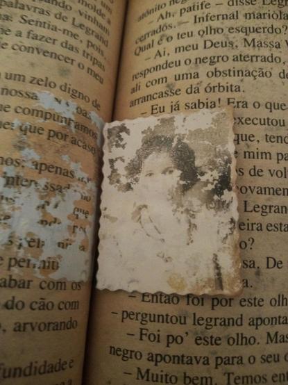 Interior do livro, página amarelada, gasta e suja. No centro uma foto 3x4 em preto e branco de uma mulher de cabelo curto, a foto está gasta e sua boca e nariz não são visíveis mas seus olhos são marcantes.