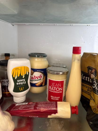 Inside of a fridge showing a jar of Calvé, a tube, two jars of Jean Baton and a bottle of Kewpie mayonnaise and a small bottle of McDonalds fries sauce.