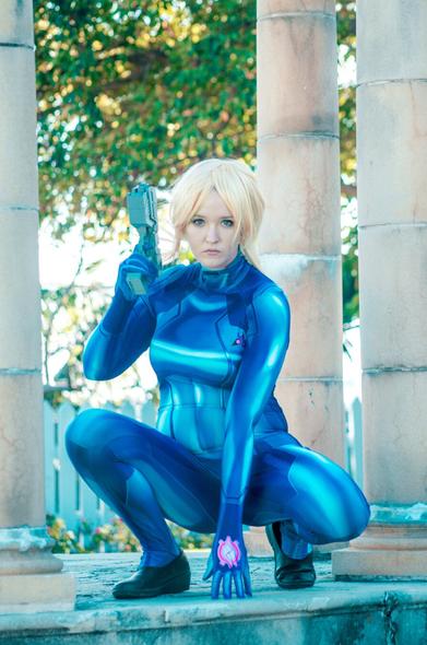 SJ Slays as Zero Suit Samus from Smash Bros crouched holding a prop weapon.