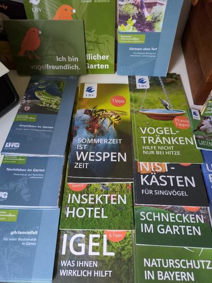 Das Bild zeigt eine Sammlung von Broschüren und Flyern, die sich mit der Umwelt und der Biodiversität im Garten befassen. Die Broschüren sind hauptsächlich in deutscher Sprache und tragen den Titel "gArtenvielfalt" und "Naturschutz in Bayern". Sie behandeln Themen wie "Amphibien im Garten", "Nachtleben im Garten", "Sommerzeit ist Wespzeit", "Insektenhotel", "Ich bin vogelfreundlich", "Gärten ohne Torf", "Vogel-Tränken", "Nistkästen für Singvögel", "Schnecken im Garten" und "Igel – was Ihnen wirklich hilft". Die Broschüren sind von der LBV (Landesverband Bayern für Vogelschutz) und anderen Umweltorganisationen herausgegeben und bieten Tipps und Praxisbeispiele für den Naturschutz im Garten. Die Farben der Broschüren sind hauptsächlich grün und blau, was auf die Natur und die Umwelt hinweist.