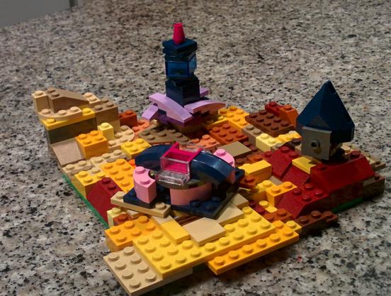 Vista aérea de un paisaje hecho con lego, no muy grande, de unos 15x15 centímetros de bases amarillas y edificios azul oscuro. Está sobre una encimera de granito.