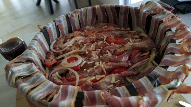 ein Dopf voll mit eingeschichtetem Fleisch, der Speck hängt noch über den Rand heraus