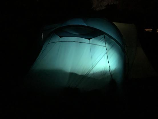 Es ist dunkle Nacht. Durch die Beleuchtung im Inneren sieht man die leicht gewölbte, bläulich schimmernde Oberfläche eines Zeltes von außen.