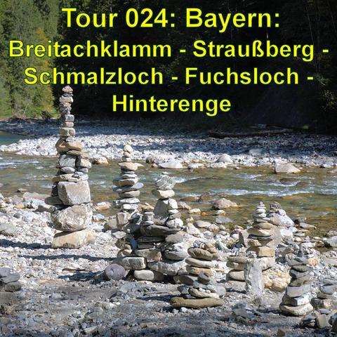 Das Bild zeigt einen Fluss mit klarem Wasser, umgeben von einem Kiesbett, auf dem mehrere Steinmännchen sorgfältig aufgeschichtet sind. Im Hintergrund sind Bäume zu erkennen, die auf einen umliegenden Wald hinweisen.