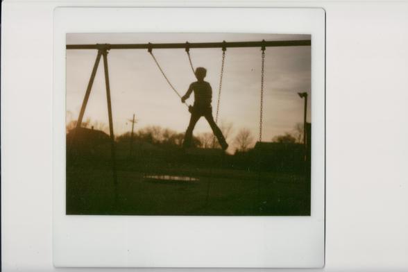 Child suspended in air on a wing. Open merry go round int he distance. Taken at sunset so everything is darkened.