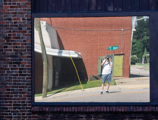 A photo of a mirrored window on a building in downtown Danville, Virginia reflecting the street and building opposite as well as yours truly taking the photo.  The distortions in the glass are reminiscent of carnival funhouse mirrors.