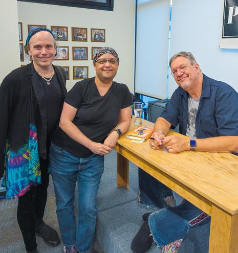 Ziggy and Pax stand next to Penn Jillette, seated and signing books at a table in a bookstore.