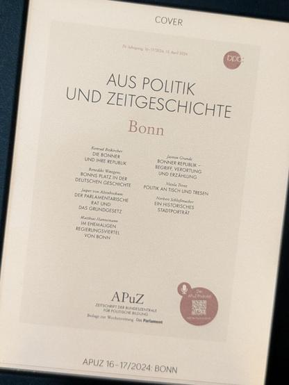 Ein E-Book-Reader zeigt die Titelseite der Zeitschrift âAus Politik und Zeitgeschichteâ (APuZ), Ausgabe 16â17/2024 mit dem Schwerpunktthema âBonnâ. Auf dem Deckblatt sind BeitrĂ€ge und Autorennamen aufgelistet, darunter Titel wie âDIE BONNER UND IHRE REPUBLIKâ, âBONNS PLATZ IN DER DEUTSCHEN GESCHICHTEâ und âPOLITIK AN TISCH UND TRESENâ. Am unteren Rand steht der Herausgeber âBundeszentrale fĂŒr politische Bildungâ.