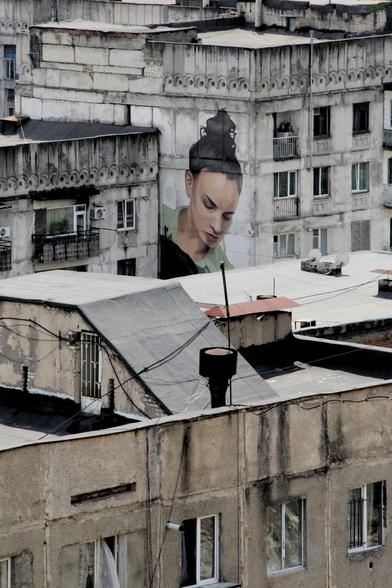 Inmitten von Häuserwänden aus Beton stellt ein Grafito eine Frau dar, die nach unten schaut.