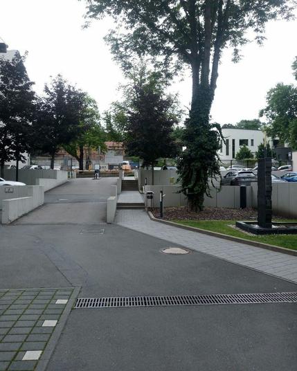 Eine rampenförmige Ausfahrt mit Schranken. Ein paar Bäume. Ein Stück corporate art.