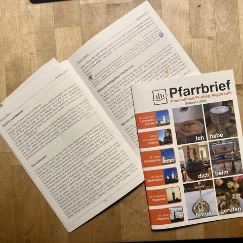 Ein Foto: Auf einer gefugten Holzunterlage liegen zwei Din-A5-Hefe, eines aufgeschlagen, eines geschlossen, sodass der Titel zu sehen ist. Auf dem Titel steht „Pfarrbrief“ und „Pfarrverband Prutting-Vogtareuth, Sommer 2025“. Darunter sind sechs Bilder von Tauforten, und in jedes ist ein Wort einmontiert. Zusammen ergibt sich: „Ich habe dich beim Namen gerufen“. An der linken Seite des Titels sind in Briefmarkengröße sechs Pfarrkirchen abgebildet und beschriftet – das sieht aus wie orange Griffreiter. Das aufgeschlagene Heft zeigt zwei Textseiten ohne Bilder. Die Überschriften der Beiträge sind gut zu erkennen: „Ayesha und Maryam“, „Pax et bonum!“, „Viktualia Rollgardina Pfefferminz“ und „Wer bin ich“. Der Pax-et-bonum-Beitrag ist mit Johanna-Jessica OSF gezeichnet. Ganz klein ist dazu das Tau der Franziskanische Familie abgebildet, ebenso das violettblaue Mastodon-Logo.