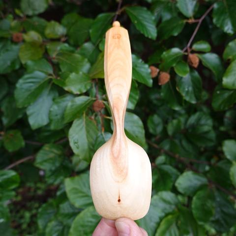 Back of wooden spoon held with leaves in the background