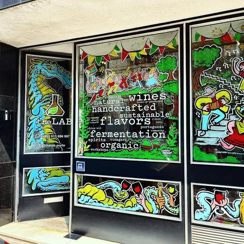 Storefront windows decorated with colorful illustrations of people dancing, a dragon, and wine; text advertises natural, handcrafted, organic Portuguese wines and flavors.