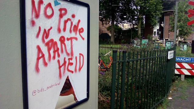 spoorwegovergang met groen hek en gras en muur met bord: no pride in apartheid @bds_nederland