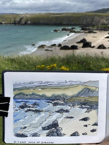 A beach with green and blue water and some darl rocks, in the foreground a aketchbook with a coloured drawing of it.