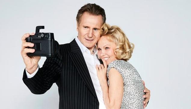 Liam Neeson y Pamela Anderson posando juntos y sonriendo mientras toman una selfie.