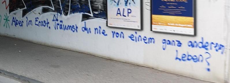 Foto blauer Handschrift auf Mauer: "Aber im Ernst, träumst du nie von einem ganz anderen Leben?"