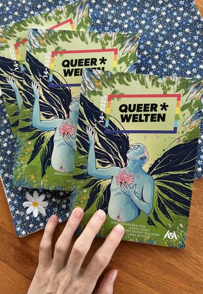 Das Bild zeigt mehrere Kopien der Publikation "QUEER* WELTEN 14" auf einer Holzoberfläche. Die Cover zeigen lebendige Kunstwerke, die eine Figur mit blauer Haut, Brille, einem rosa Haarschatten und großen schwarzen Flügeln darstellen, die eine rosa Blume in der Hand hält.