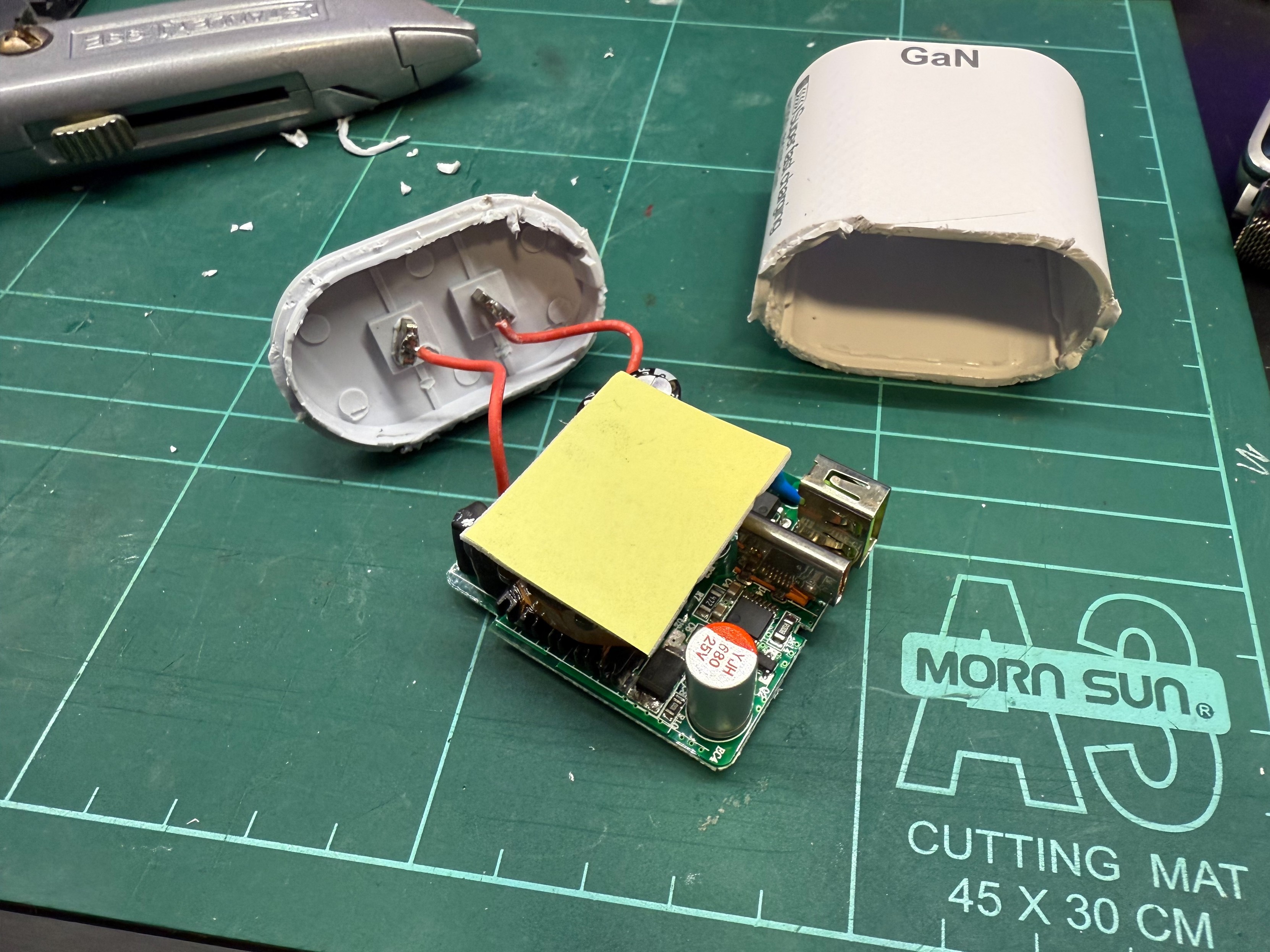White plastic USB charger with the chassis cut open showing a PCB under foam piece