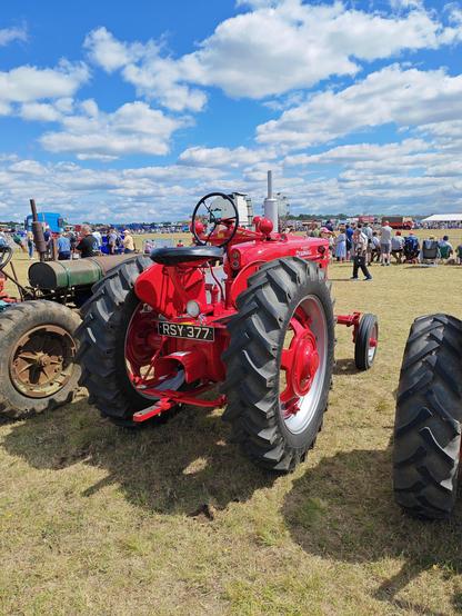 A big red tractor without a cab. The wheel is cold steel, as is the seat