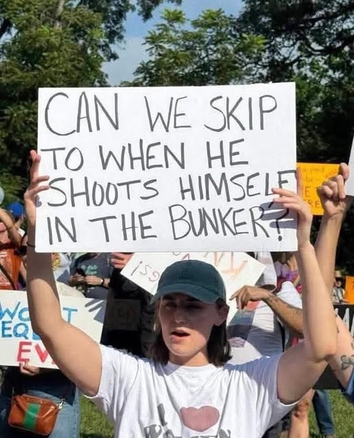 The picture is of a protester with a sign reading, "Can we skip to the part where he shoots himself in the bunker?"