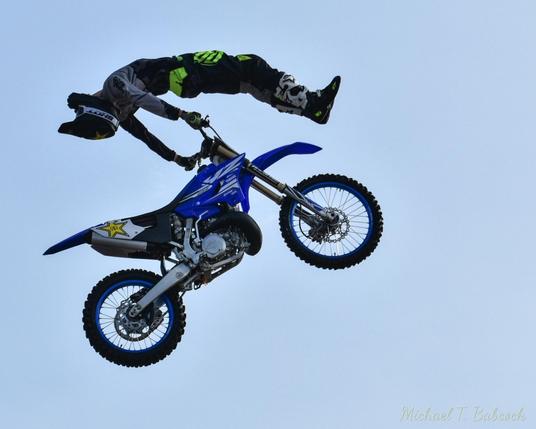 A mid-air motorcyle with the rider floating above it, hands on the handlebars from behind themselves, feet over the front wheel.