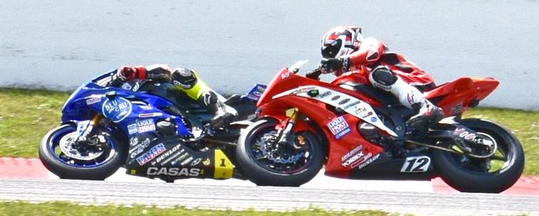 Two superbikes going around a corner in a full lean, one red and one blue.