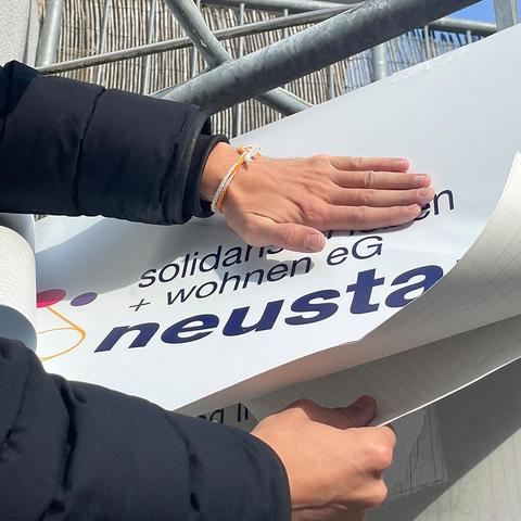 Noch nähere Nahaufname: Anbringen der Folie mit dem Logo der Genossenschaft neustart solidarisch leben + wohnen eG