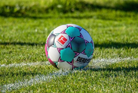 Ein bunter Derbystar-Fußball liegt auf einer weiß gekalkten Linie auf einem grünen Grasplatz.