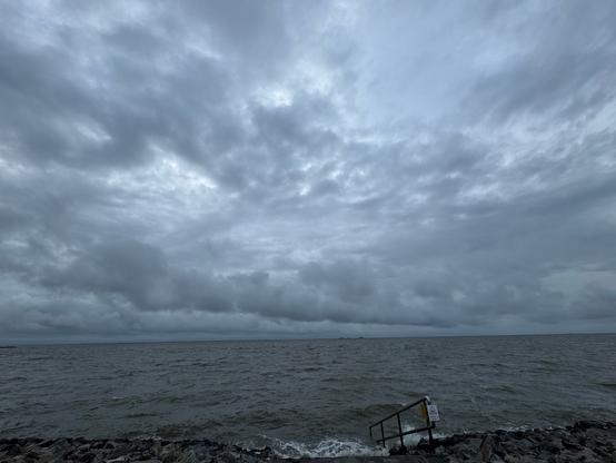 A wavey North Sea under a cloudy sky. A steel railing lead into the water.