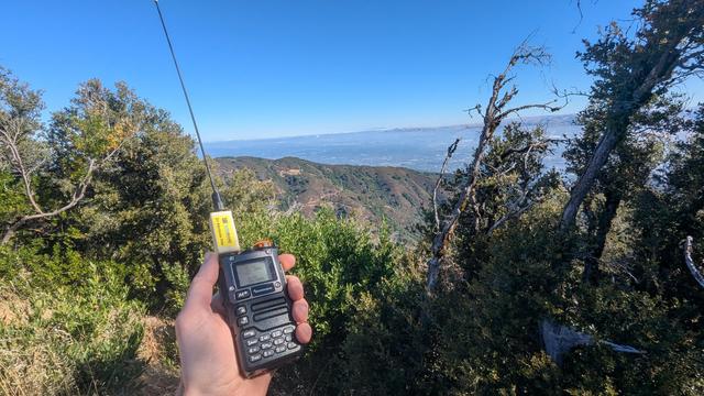 A hand holding a Quansheng uv-k5 with a band pass filter on it. In the background below is silicon valley, mostly out of the fog.