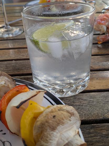 A gimlet in a rocks glass with a plate that has a skewer with mushrooms, bell pepper, and onion