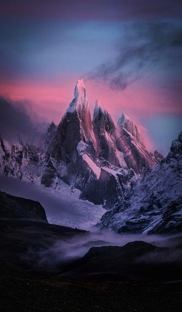 the Cerro Torre mountain range in Argentina is shown at sunrise with what are basically the trans flag colors and some clouds. no ai used ofc