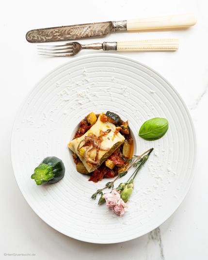 Weiße Marmorplatte. Darauf ein kleiner, runder, weißer Pastateller. Darin italienische Maultaschen mit Auberginen, Zucchini und weiterem Gemüse gefüllt.