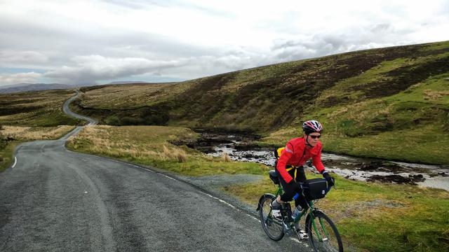 Man riding a bike on Skye, road twisting into the distance.