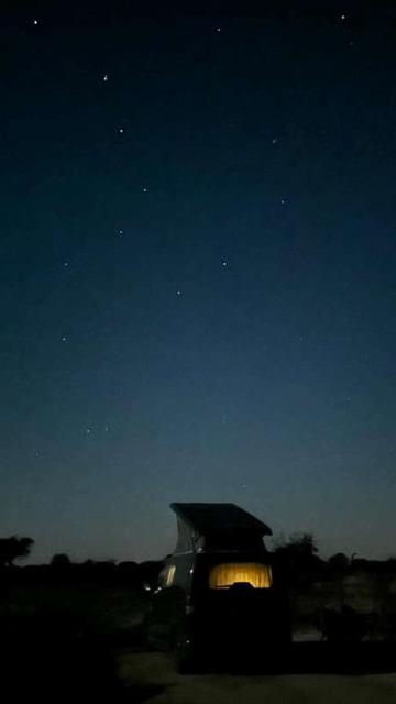 A cozy small campervan under a vast, star-filled night sky at Bubulcus & Bolotas. The warm glow from inside the van contrasts beautifully with the dark, peaceful surroundings and the sparkling constellations above.