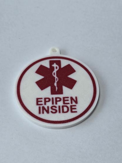 a 3d printed white & round sign, with red lettering and symbol showing the words "epipen inside" and a medical icon