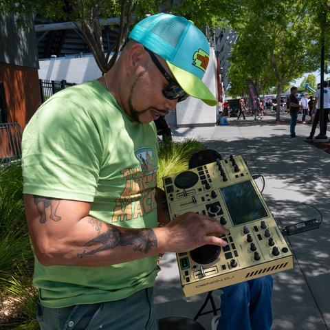 A man in a Mystery Machine shirt and baseball hat operating a wireless DJ deck