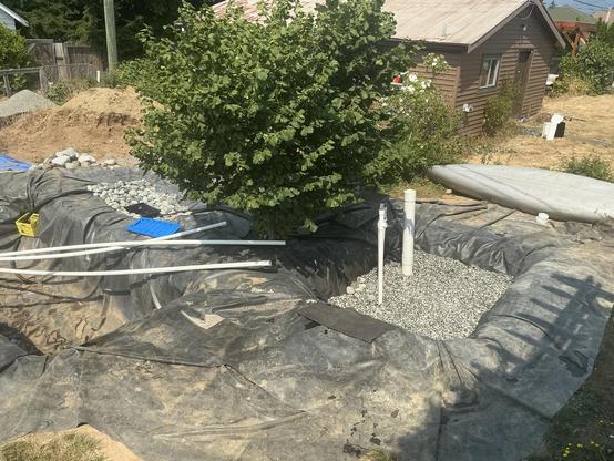 A view from the deck of the three holes shows the nearest one, square shaped, with two white pipes jutting out, about 2/3 full with rock.