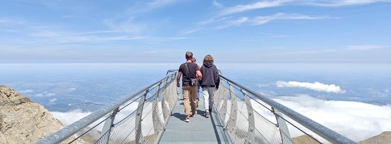 Photo de ma famille, de dos, avançant sur une passerelle au dessus du vide. Il y a des nuages en dessous, si bien qu'on semble aller vers le ciel.