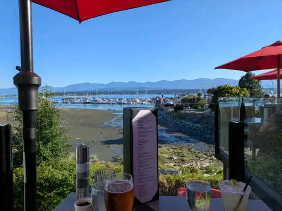 looking out across comox harbour from a pub's outdoor patio. Vancouver Island's mountains are in the background, there are boats in the marina close by and you can see some drinks on a table in the foreground