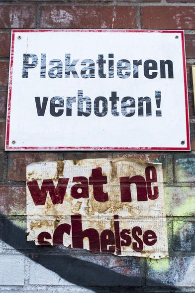 farbfotografie, hochformat. auf einer roten ziegelsteinmauer oben ein weißes schild mit rotem rand und der aufschrift: plakatieren verboten! darunter ein blatt mit der aufschrift: wat ne scheiße.

color photograph, portrait format. on a red brick wall, at the top, a white sign with a red border and the inscription: no posting! below it, a sheet of paper with the inscription: what a load of crap.