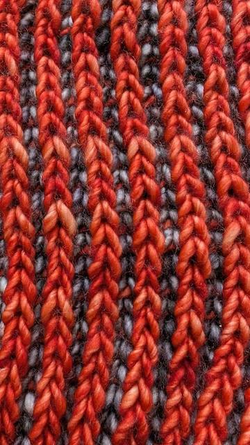 Close-up view of the hand-knit cowl. The cowl is made of two colors of yarn: an orangey red and a silvery gray. Both colors are variegated and get lighter and darker.