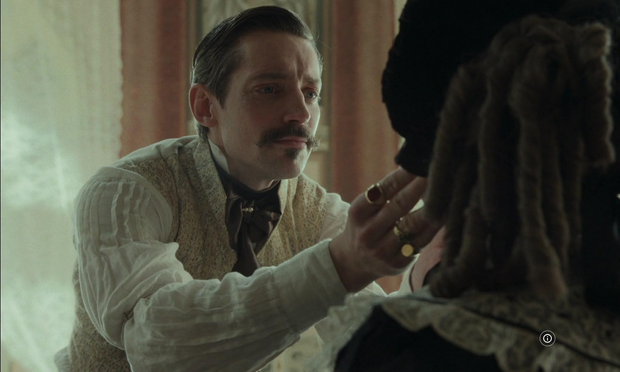 Scène de The Ugly Stepsister. Adam Lungren dans le rôle du Docteur Esthétique, examinant Elvira (que l'on voit de dos avec ses bouclettes victoriennes).
Cheveux bruns grisonnant gominés en petite vague sur le côté, yeux bleus, grand moustache et petit bouc. Cravate veste et chemise bouffante façon Second Empire. Bagues sur presque tous les doigts.