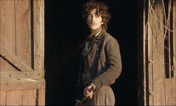 Scène de The Ugly Stepsister : Malte Gårdinger dans le rôle d'Isak le palefrenier. Il est devant l'écurie, un râteau à la main. Veste, gilet et foulards grisâtres et grossier, sa tenue a plusieurs rangées de boutons. Moustache d'adolescent à peine pubère, grands cheveux bruns frisés tombant presque en mulet, yeux clairs grand ouvert.