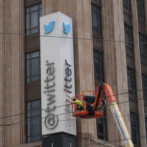 A worker on a crane removes the letters of a “Twitter” sign from the side of a building.