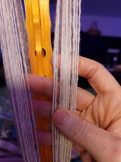 Thin yarn wound onto a yellow plastic niddy-noddy, with my fingers for scale.